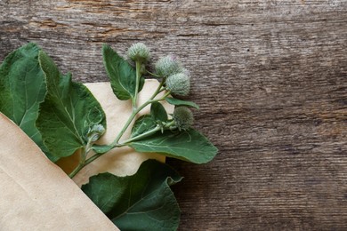 Photo of Fresh green burdock leaves and flowers in envelope on wooden table, top view. Space for text
