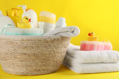 Photo of Basket with baby cosmetic products and accessories on yellow background