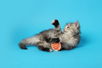 Photo of Cute kitten playing with ball on light blue background