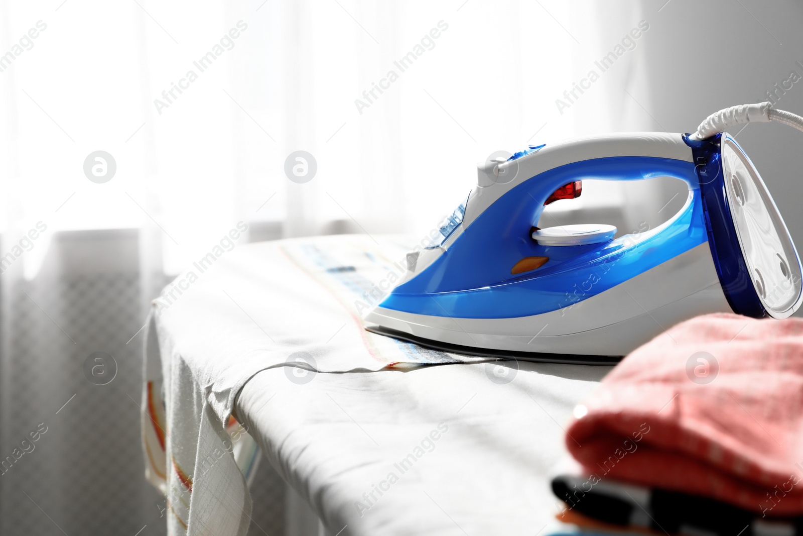 Photo of Modern electric iron on board indoors, space for text. Household appliance