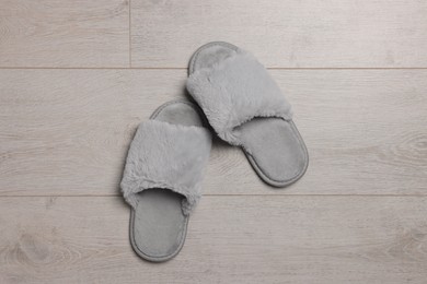 Photo of Pair of soft grey slippers on wooden floor, top view