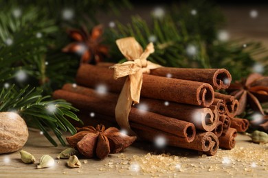 Different spices and fir tree branches on wooden table, closeup. Cinnamon, anise, cardamom, nutmeg