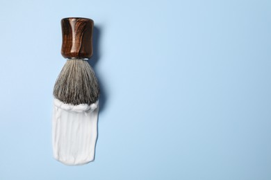 Photo of Brush with shaving foam on light blue background, top view. Space for text