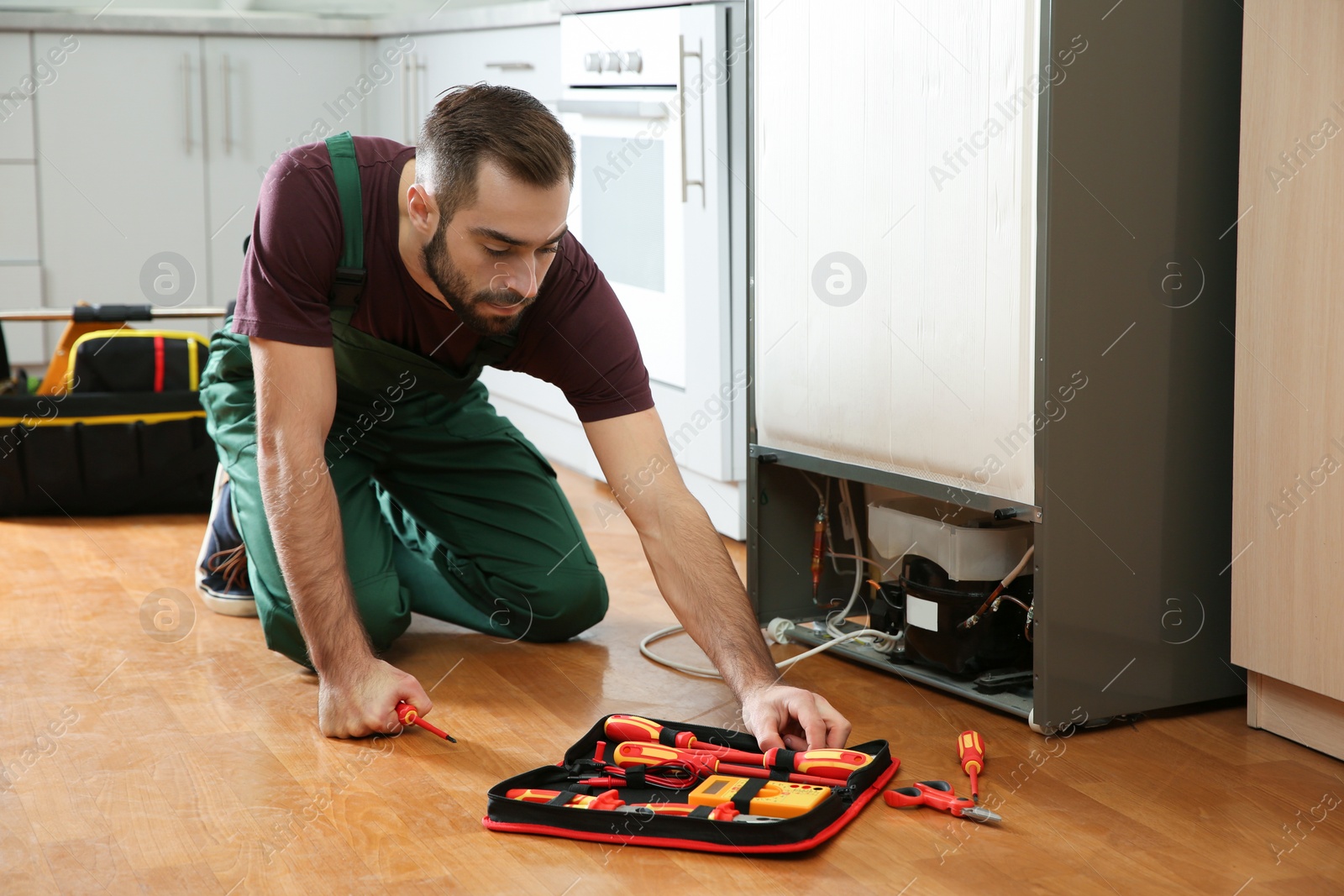 Photo of Male technician in uniform repairing refrigerator indoors