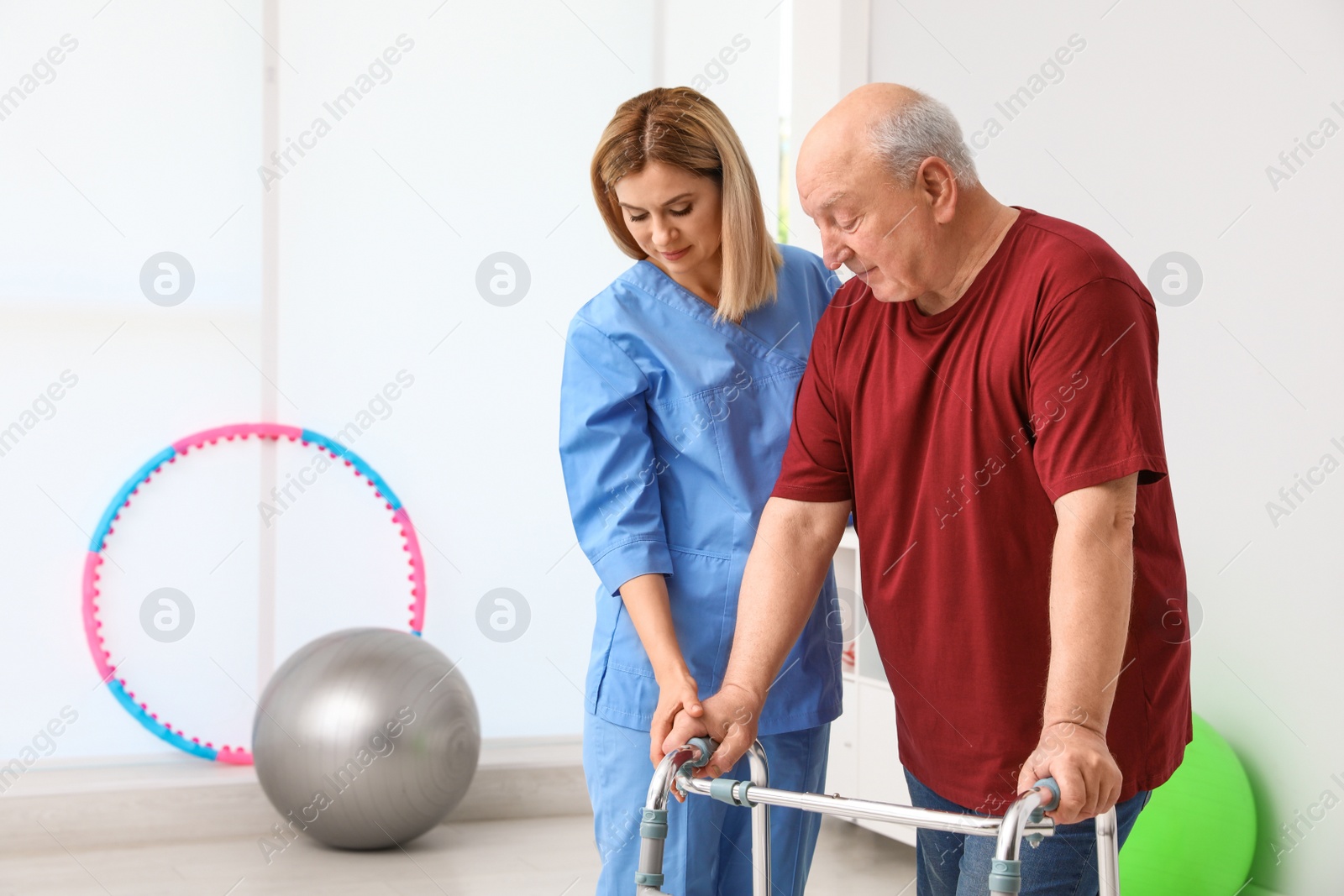 Photo of Caretaker helping elderly man with walking frame indoors