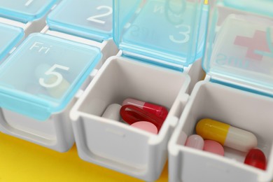 Plastic box with different pills on yellow background, closeup