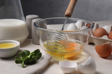 Photo of Metal whisk, raw eggs in bowl and ingredients on light table, closeup