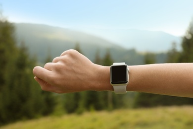 Photo of Woman checking smart watch with blank screen in wilderness, closeup