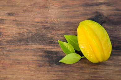 Photo of Delicious ripe carambola with leaves on wooden table, top view. Space for text