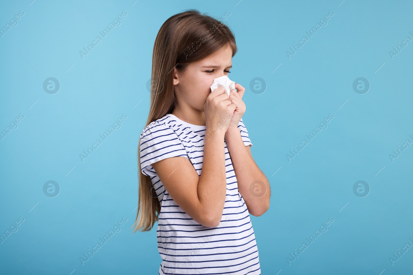 Photo of Sick girl with tissue coughing on light blue background