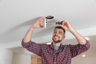 Man with screwdriver repairing ceiling lamp indoors