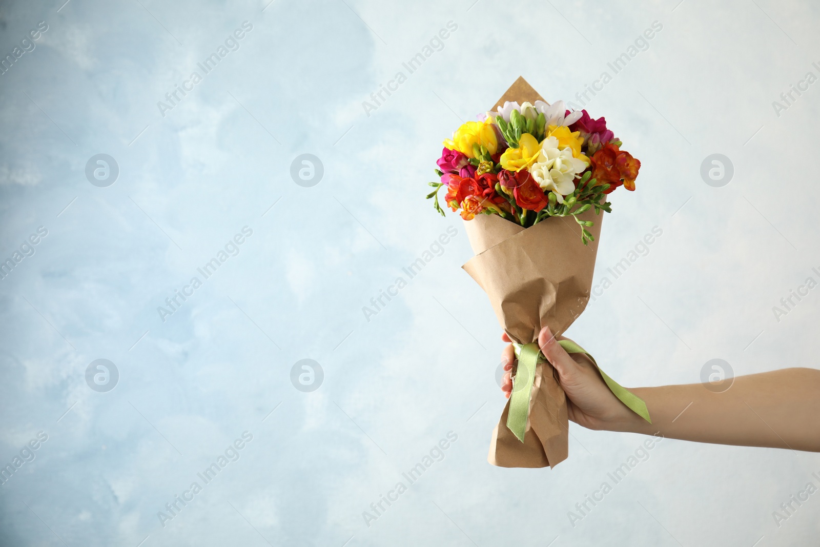 Photo of Woman holding bouquet of beautiful spring freesia flowers on color background. Space for text