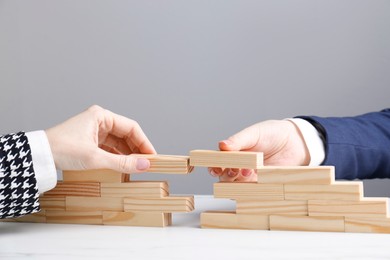 Photo of Businesspeople building bridge with wooden blocks at table, closeup. Connection, relationships and deal concept