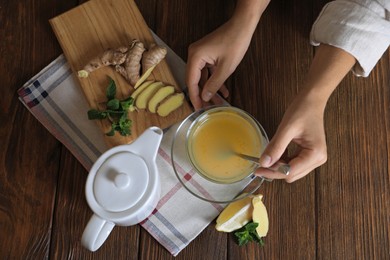 Photo of Woman making aromatic ginger tea at wooden table, top view