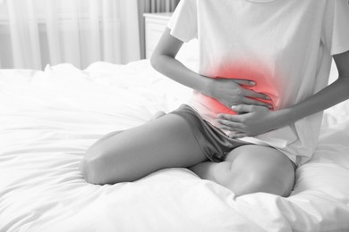 Woman suffering from abdominal pain on bed at home. Black and white effect with red accent