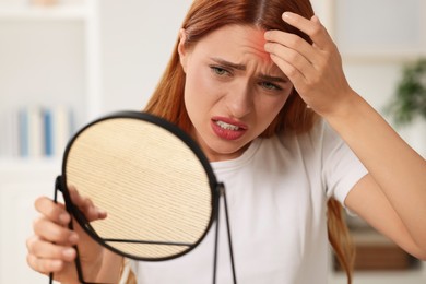Photo of Suffering from allergy. Young woman looking in mirror and scratching her face at home