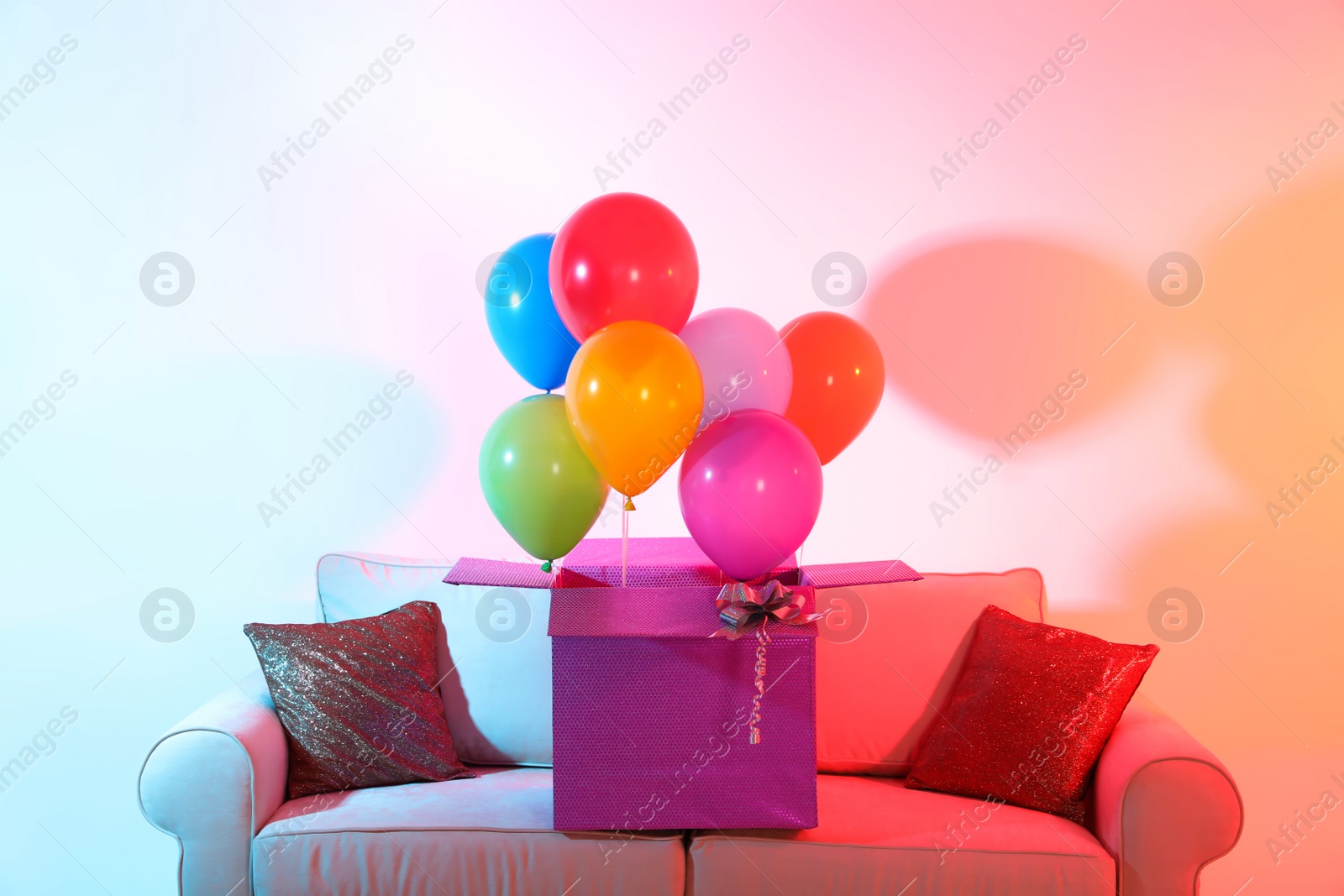 Photo of Gift box with bright air balloons on sofa against color background