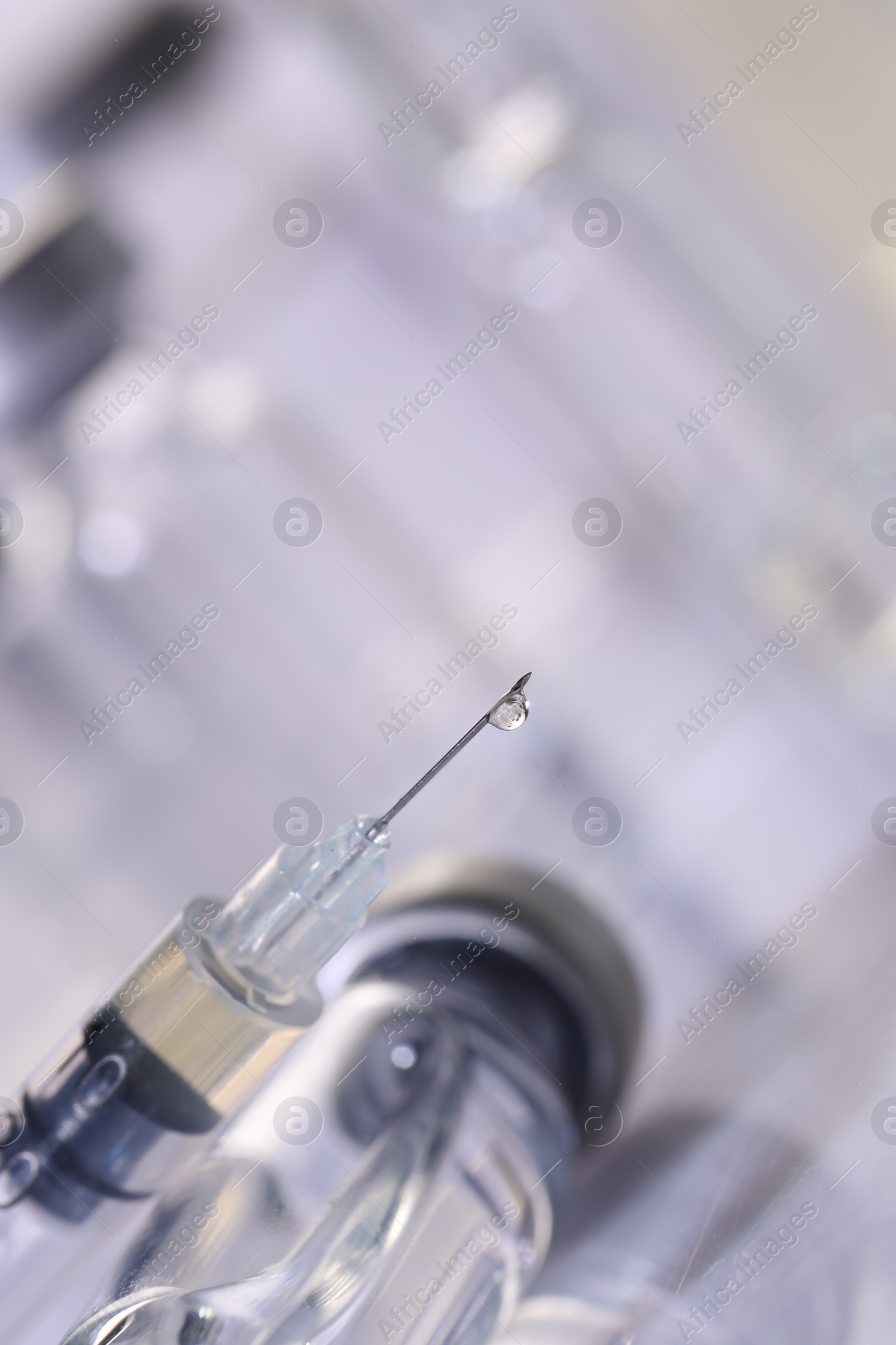 Photo of Drop of medication on syringe needle against blurred background, closeup. Space for text