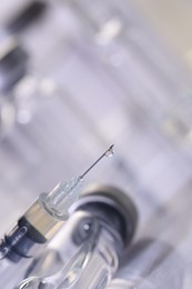 Drop of medication on syringe needle against blurred background, closeup. Space for text