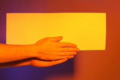 Man holding sheet of paper on color background, closeup. Mockup for design