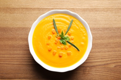 Photo of Bowl with tasty pumpkin soup on wooden table, top view