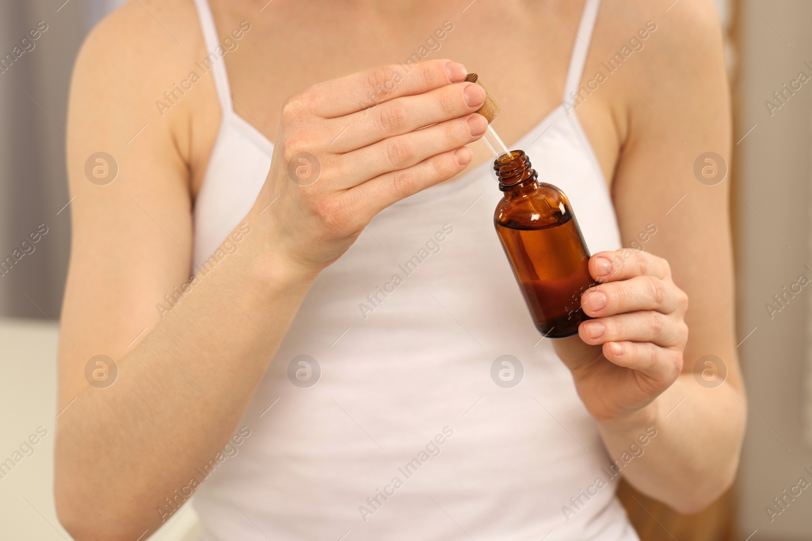 Photo of Woman with bottle of essential oil on blurred background, closeup