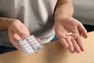 Photo of Man holding pills at wooden table, closeup