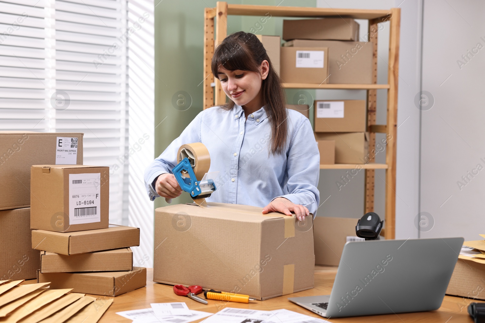 Photo of Parcel packing. Post office worker taping box at wooden table indoors