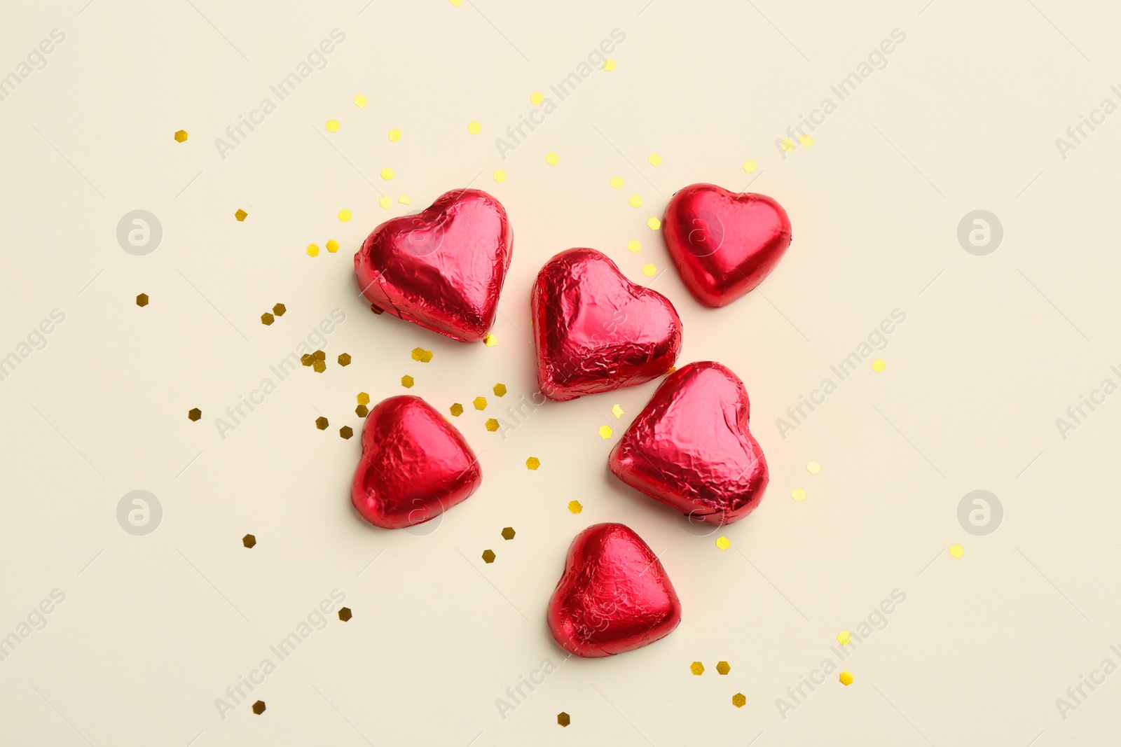 Photo of Heart shaped chocolate candies and glitter on beige background, flat lay