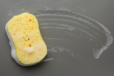 Photo of Yellow sponge with foam on grey background