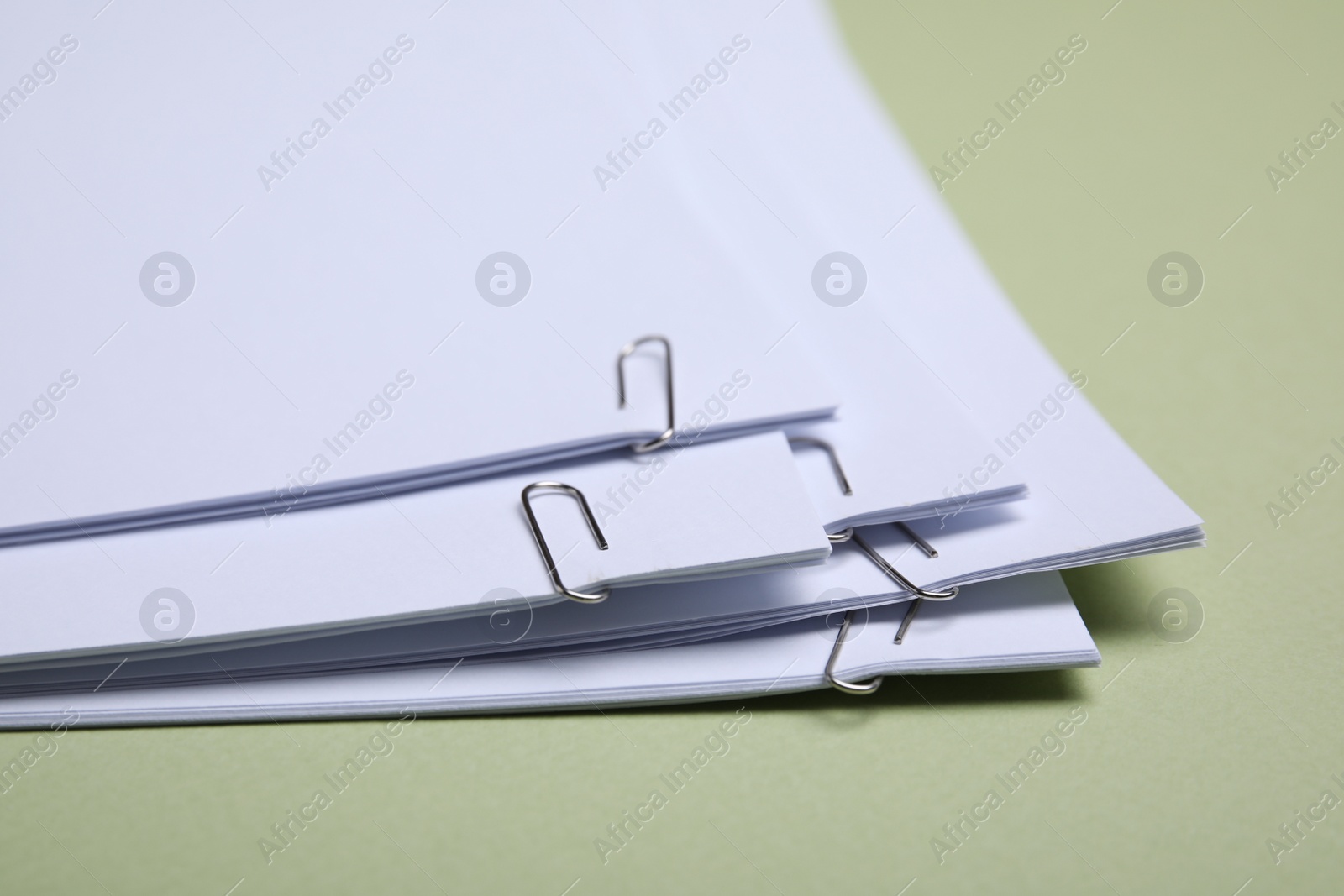 Photo of Sheets of paper with clips on light green background, closeup