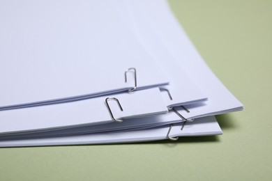 Photo of Sheets of paper with clips on light green background, closeup