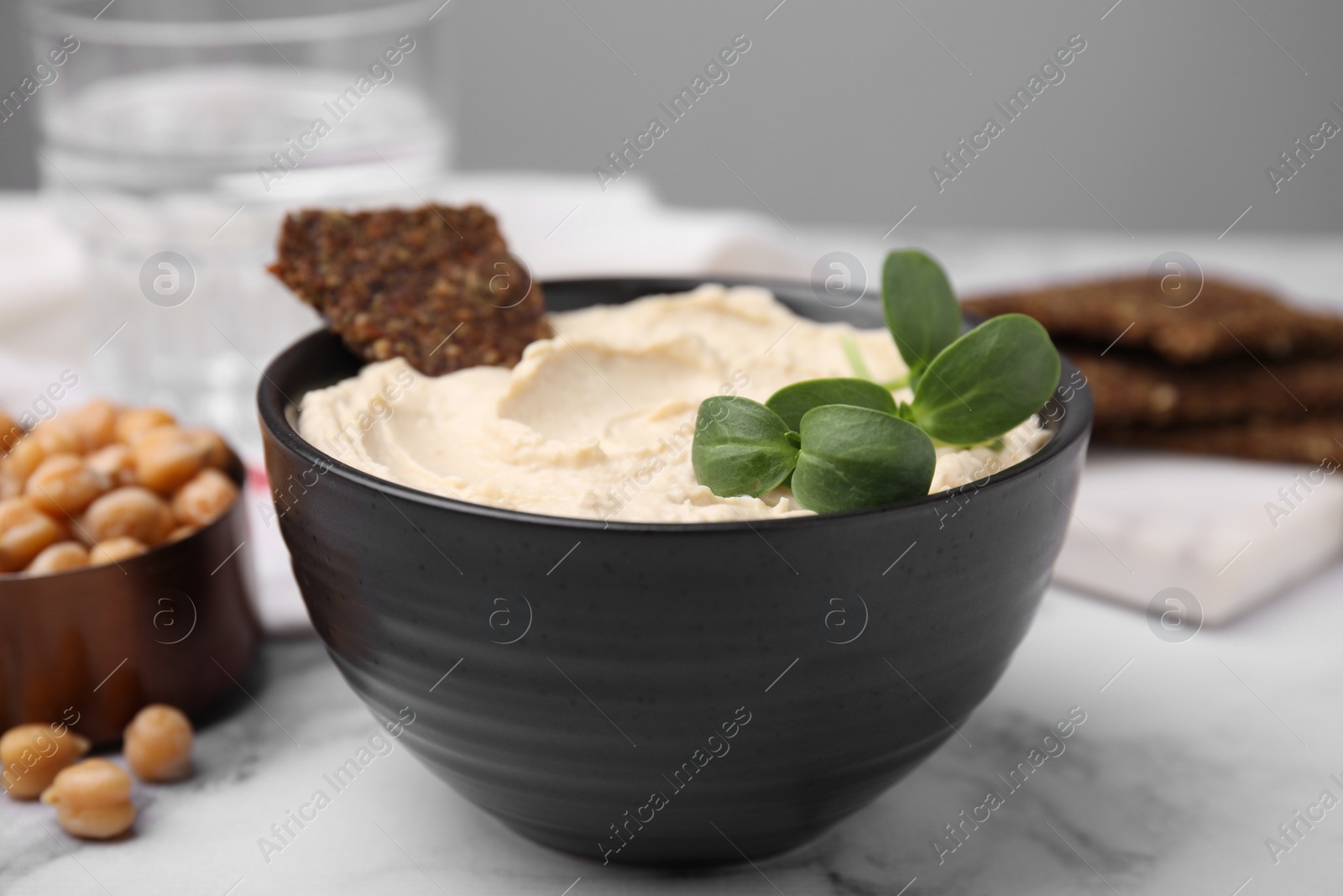Photo of Delicious hummus with crispbread served on white marble table, closeup