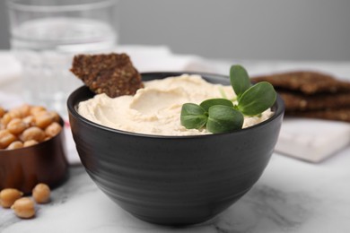 Photo of Delicious hummus with crispbread served on white marble table, closeup