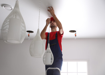 Worker installing lamp on stretch ceiling indoors