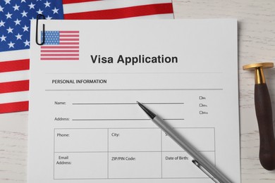 Photo of Immigration to USA. Visa application form, flag, stamp and pen on white wooden table, flat lay