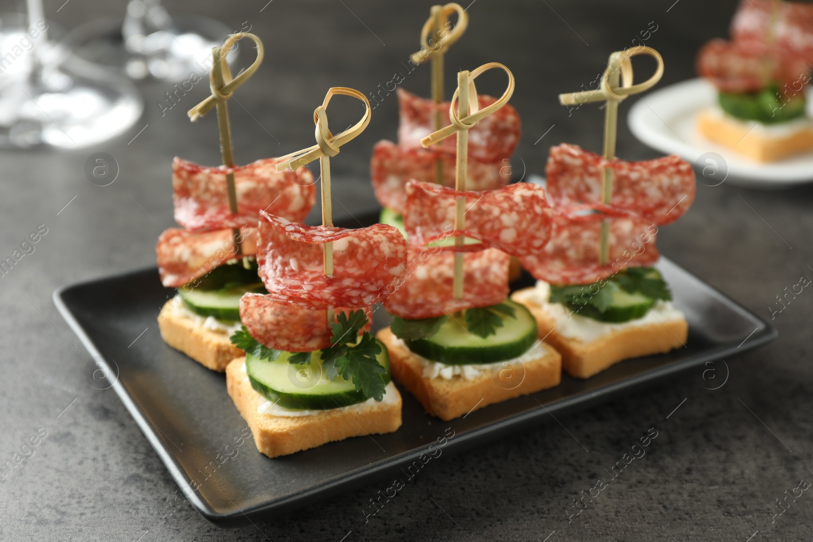 Photo of Tasty canapes with salami, cucumber and cream cheese on grey table, closeup