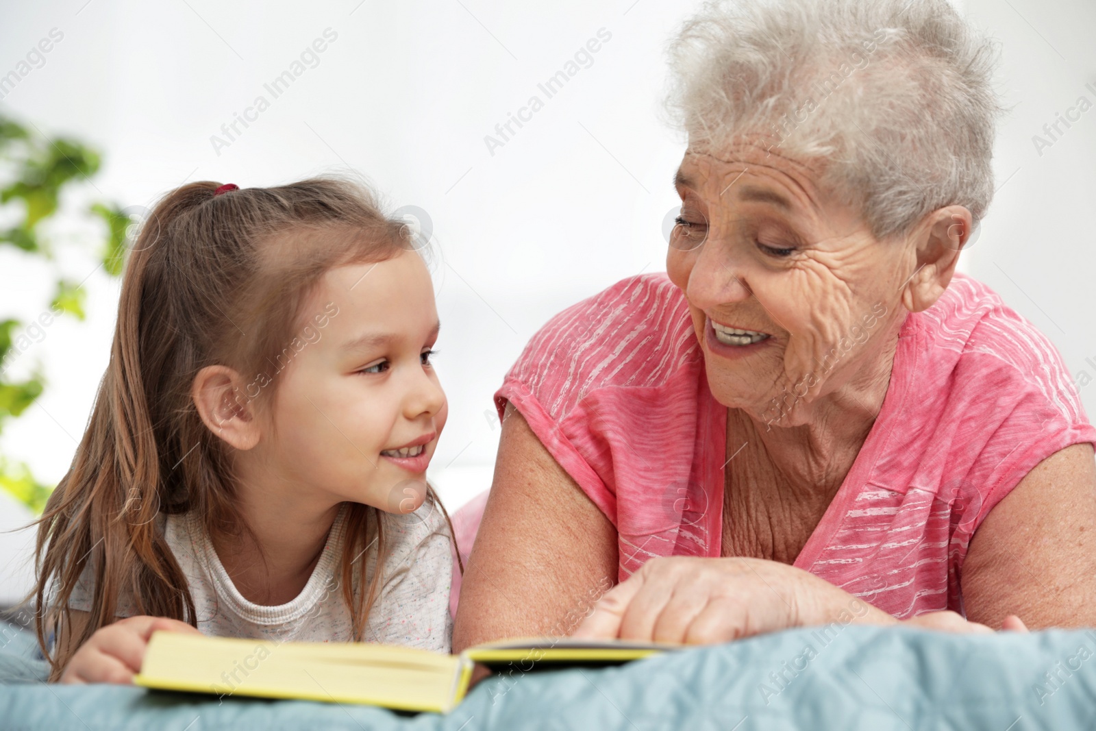 Photo of Cute girl and her grandmother reading book on bed at home