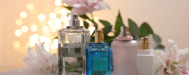 Photo of Bottles of perfume against beautiful lily flowers and blurred lights, closeup