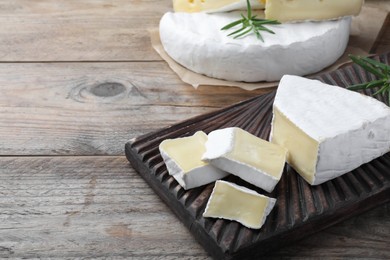 Photo of Tasty cut brie cheese with rosemary on wooden table, space for text