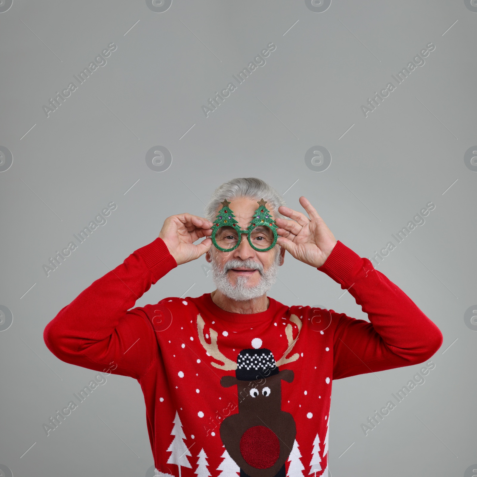 Photo of Senior man in Christmas sweater and funny glasses on grey background