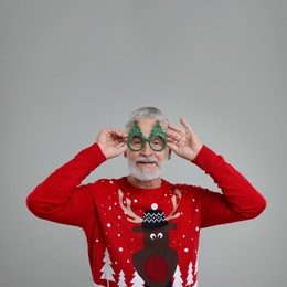 Photo of Senior man in Christmas sweater and funny glasses on grey background