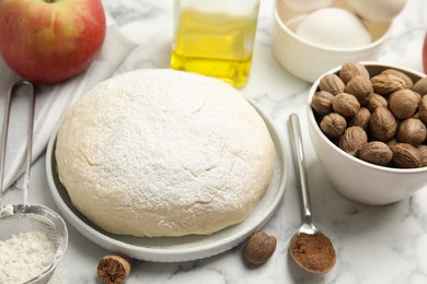Photo of Raw dough, nutmeg seeds and other ingredients for pastry on white marble table
