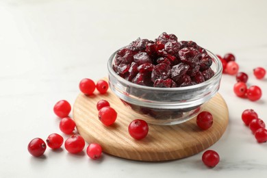 Tasty dried cranberries in bowl and fresh ones on white table, closeup. Space for text