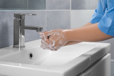 Photo of Doctor washing hands with water from tap in bathroom, closeup