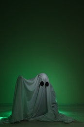 Photo of Creepy ghost. Woman covered with sheet in green light, space for text