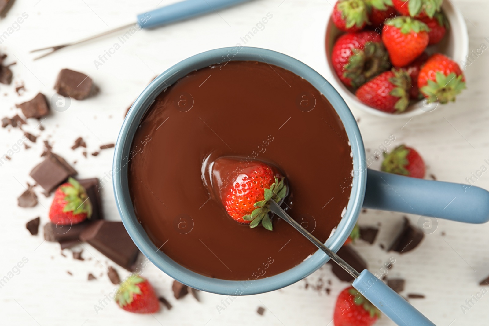 Photo of Dipping strawberry into fondue pot with chocolate on white table, top view