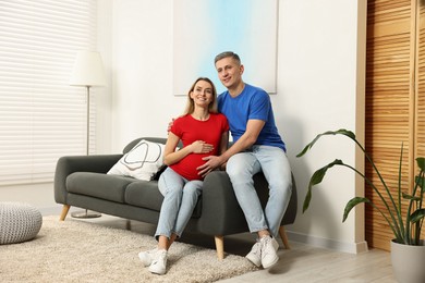 Young family housing concept. Pregnant woman with her husband on sofa at home