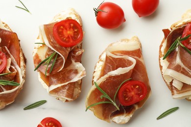 Photo of Tasty sandwiches with cured ham, rosemary and tomatoes on white marble table, flat lay