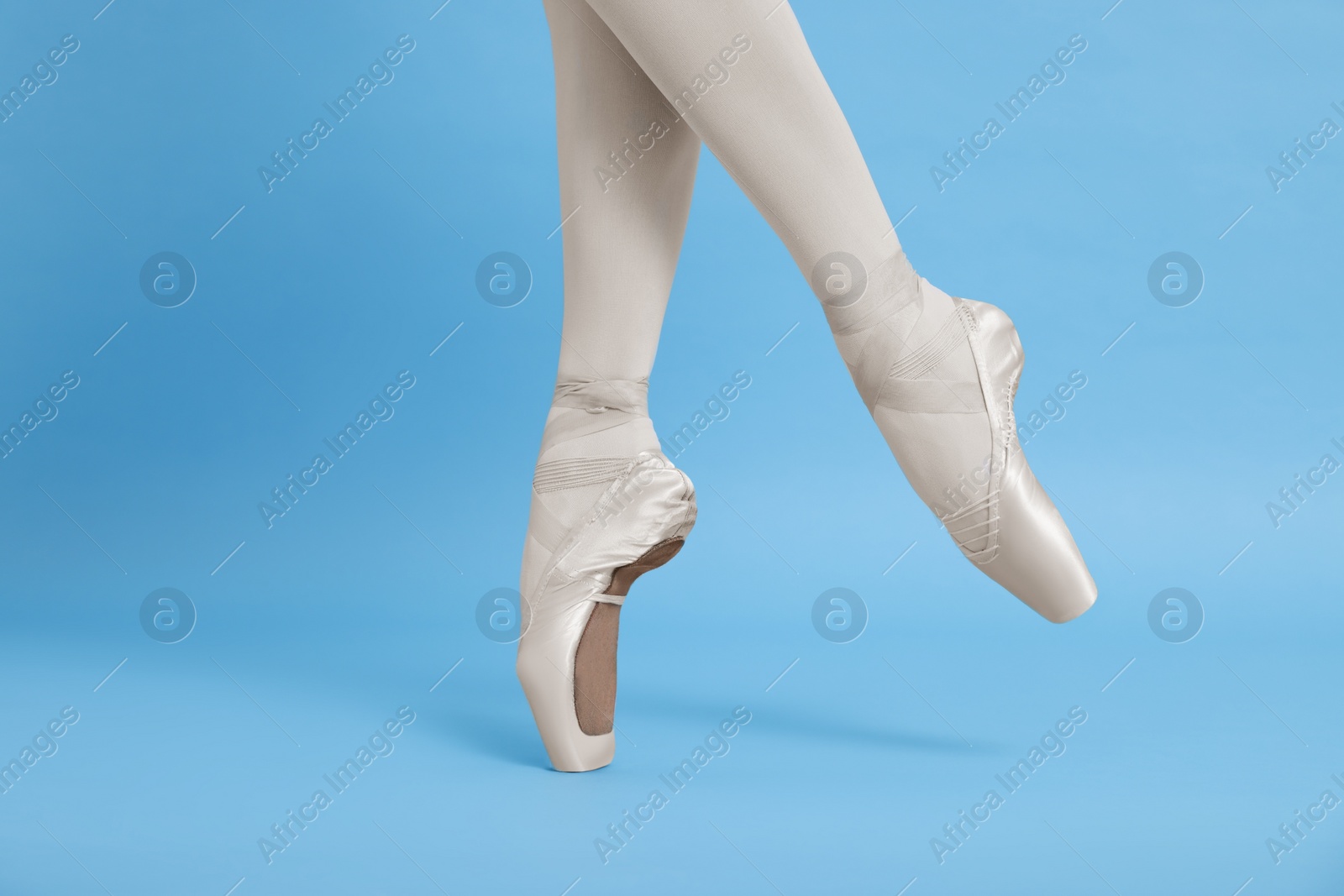 Photo of Young ballerina in pointe shoes practicing dance moves on light blue background, closeup